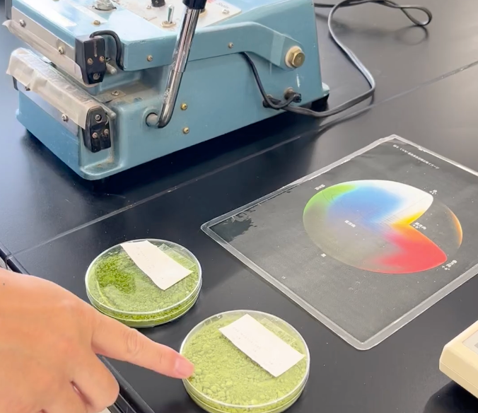 Two green matcha powder samples beside a colour chart and laboratory equipment
