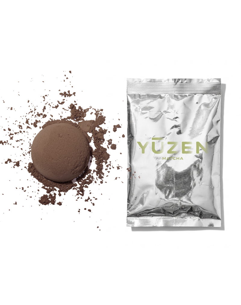 Hojicha sample in a silver foil sachet beside a pressed disc of brown roasted tea powder